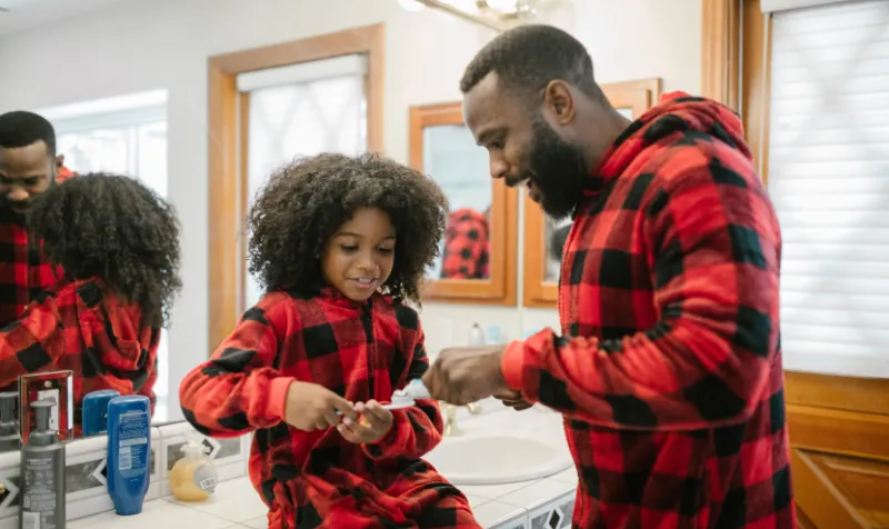 Dad helping put toothpaste on daughter's toothbrush